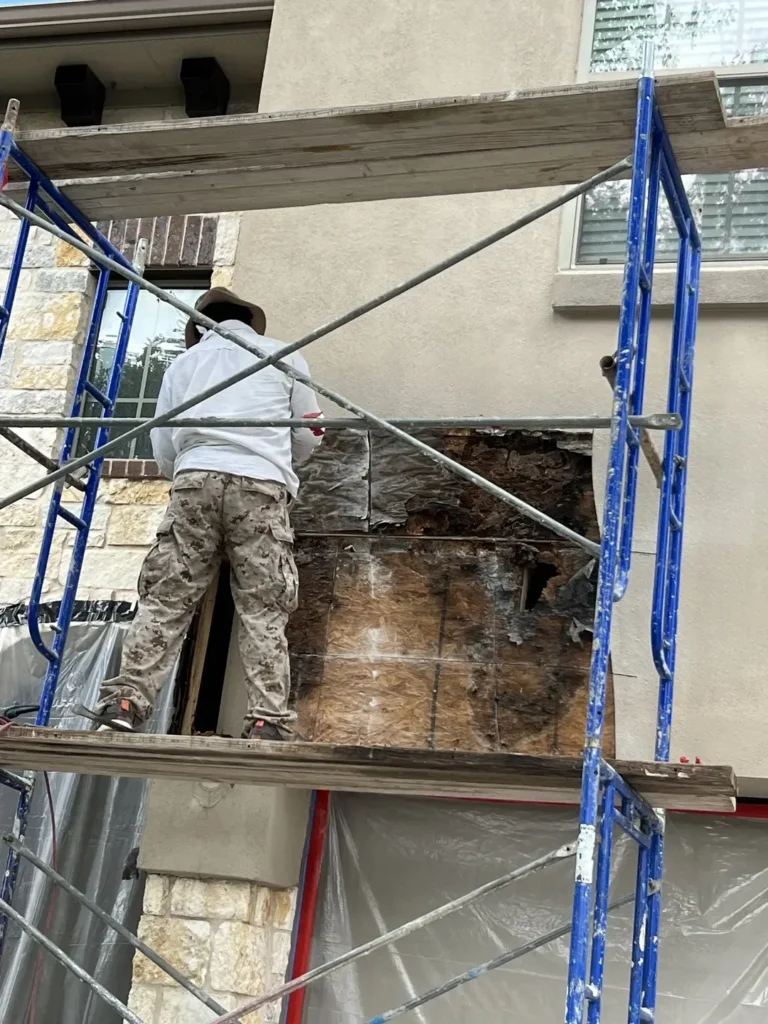 Crew member removing water-damaged sheathing from scaffolding